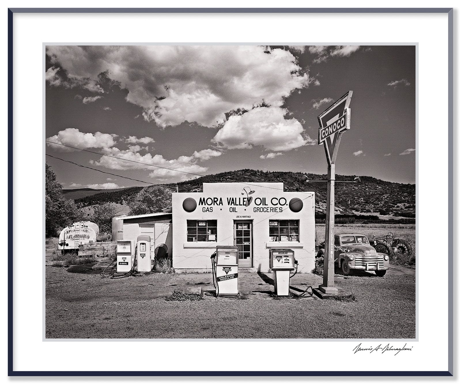 A classic black and white photograph of the Mora Valley Oil Company, a vintage gas station in rural New Mexico.