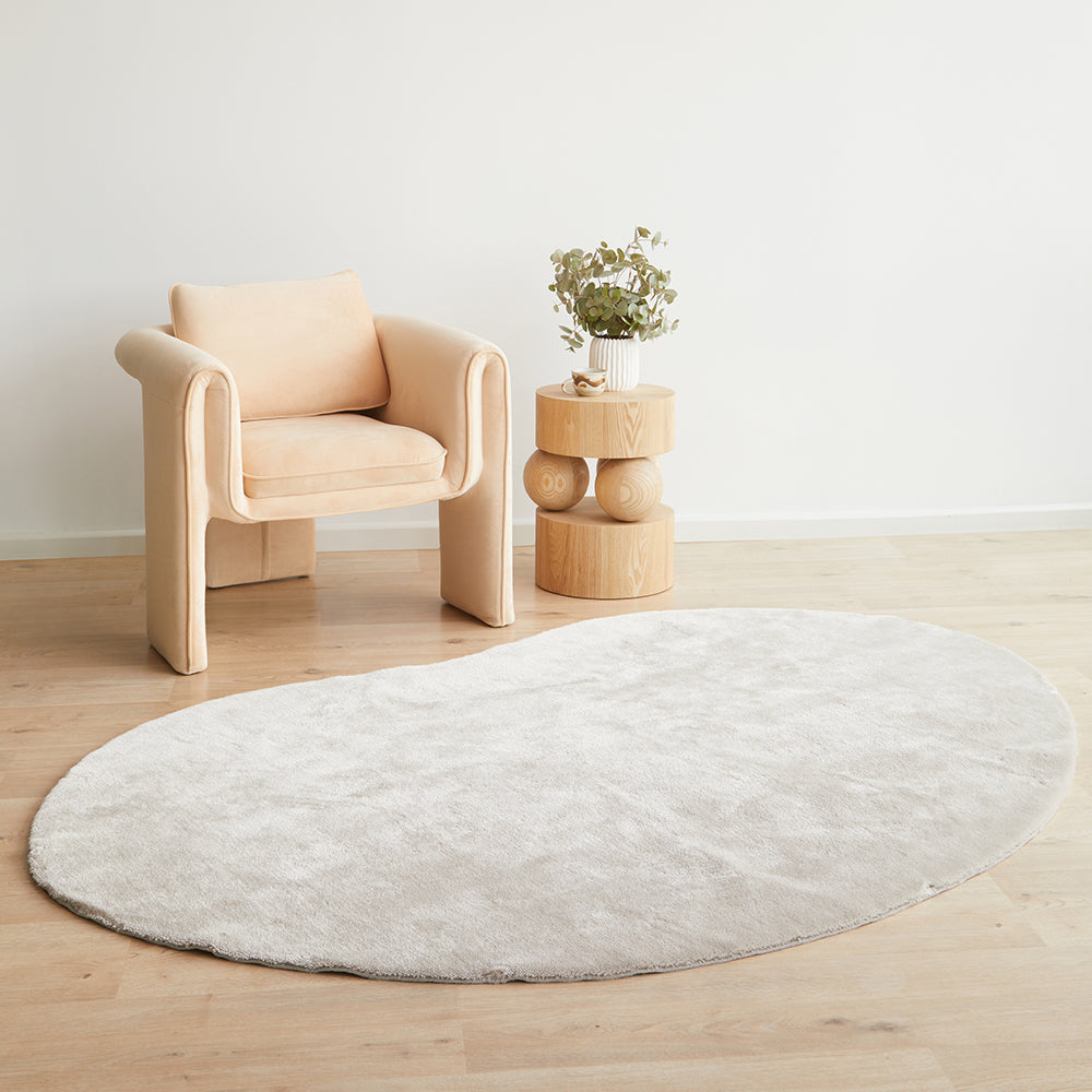 Oval pearl rug on a wooden floor with a beige armchair and small wooden table in the background.