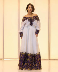 Woman wearing a white dress with black and gold embroidery against a light background