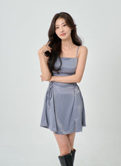 LEWKIN Silky Satin Cross Waist Tie Thin Strap Mini Dress IO27 in dusty blue, front three-quarter view on model, slim-fit silhouette with cross lace-up waist ties, paired with black knee-high boots.