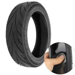 Black tire with tread pattern and a hand holding it for scale on a white background