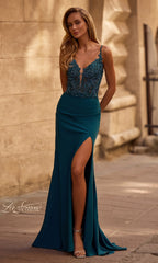 A woman in the Beaded-Corset Long Prom Dress: La Femme 33001, featuring a teal lace-up design, beaded illusion-lace bodice, spaghetti straps, and high slit, stands outdoors by a stone wall.