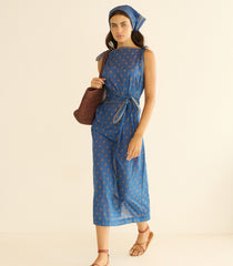 Woman wearing a blue paisley dress, holding a brown bag on a beige background