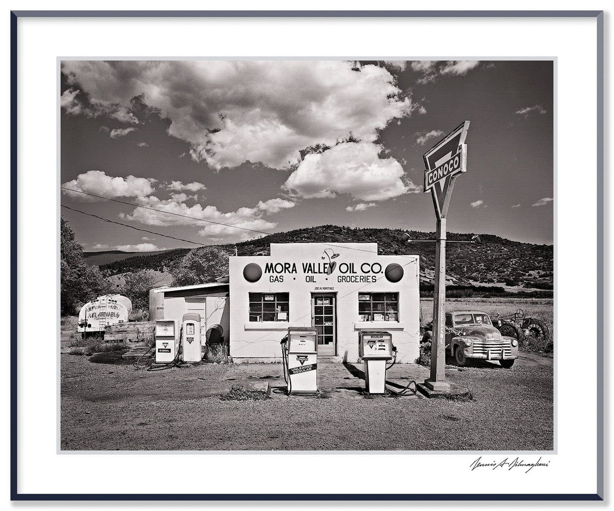 A classic black and white photograph of the Mora Valley Oil Company, a vintage gas station in rural New Mexico.