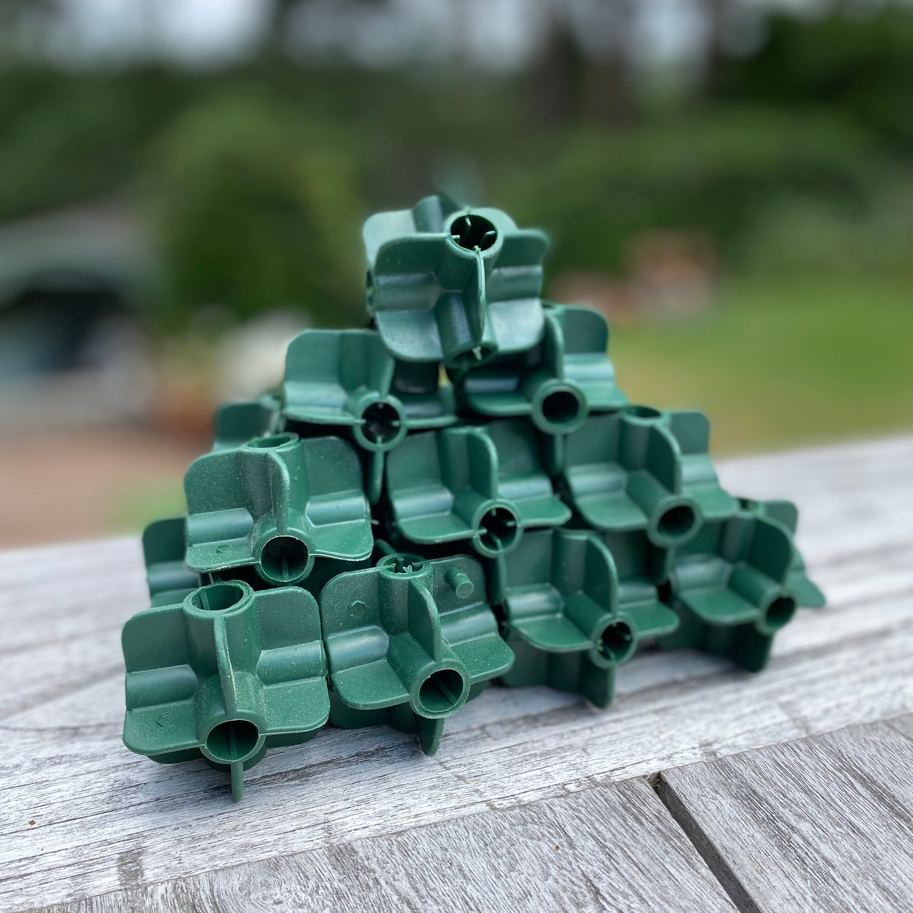 A stack of green plastic fruit cage connectors designed to hold bamboo canes for creating frames in gardens.