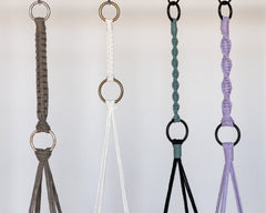 long macrame strap used to extend the length and/or lower a plant hanger. They are connected to metal rings in silver, antiqued brass and black. Two are straight and two are spiral.