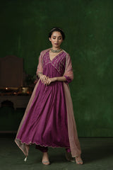 Woman wearing a traditional outfit with a purple dress and pink dupatta against a dark green background