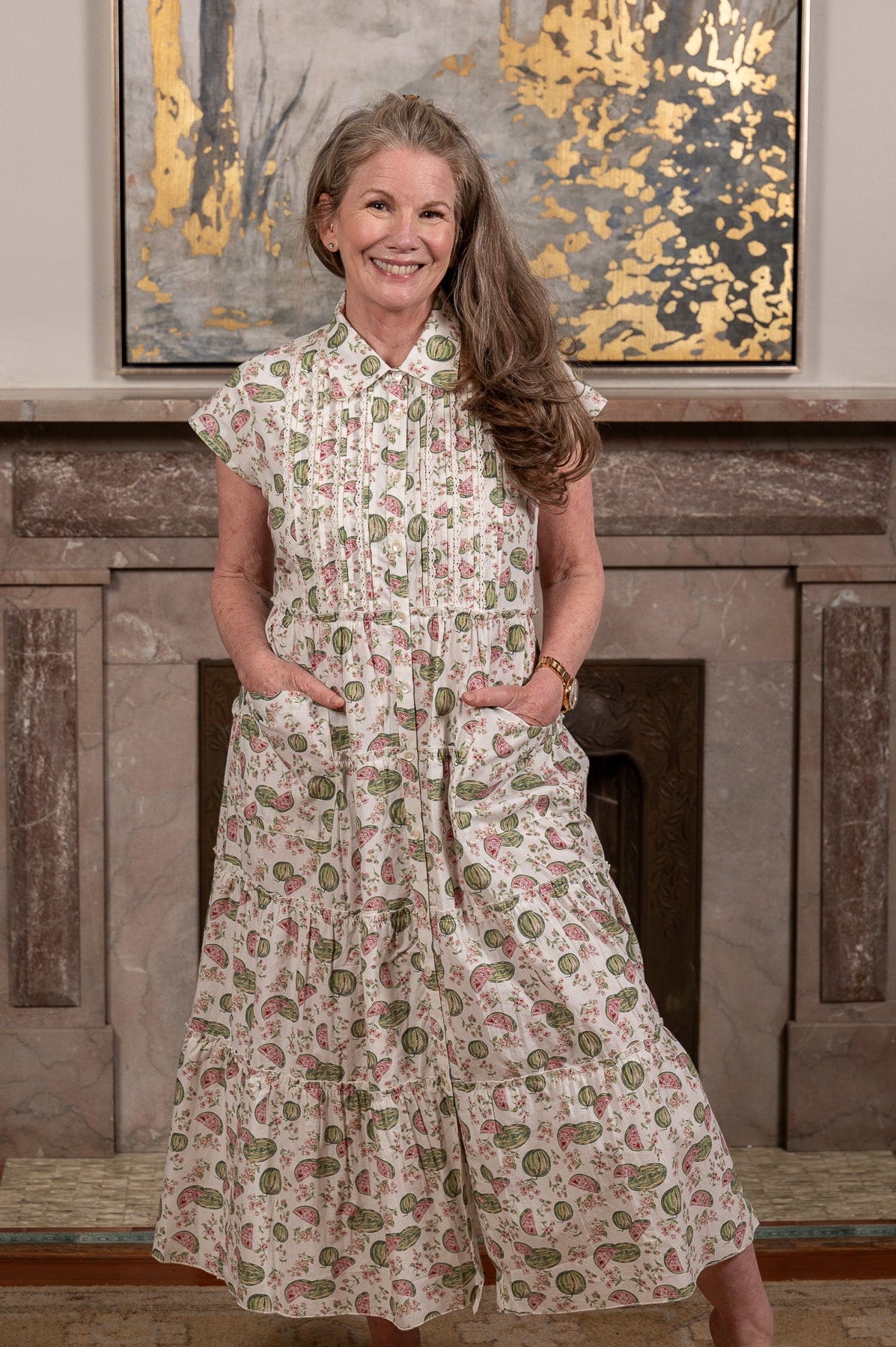 Melissa in a floral dress standing in a room with a fireplace and abstract painting.